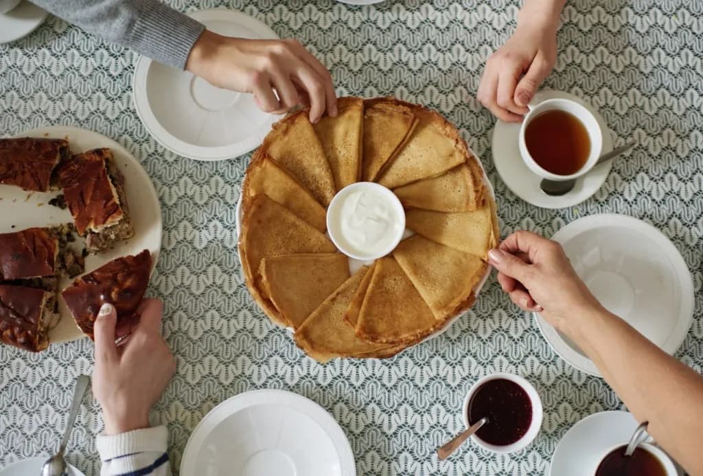 Des blinis partagés autour d’une table, avec le thé, la crème et la confiture